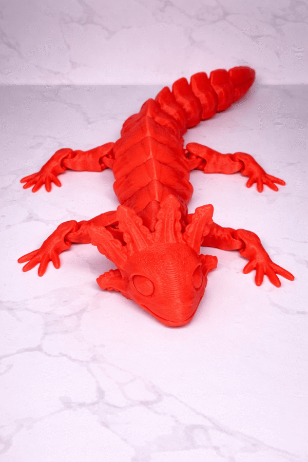 Red 3D printed Axolotl figurine with articulated joints, lying on a white marble surface